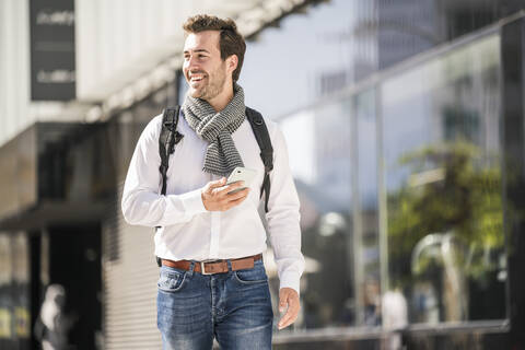 Lächelnder junger Mann mit Rucksack und Mobiltelefon in der Stadt unterwegs, lizenzfreies Stockfoto