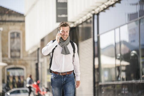 Smiling young man with backpack on the phone in the city stock photo
