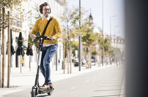 Junger Mann fährt E-Roller in der Stadt, lizenzfreies Stockfoto