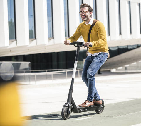 Junger Mann fährt E-Roller in der Stadt, lizenzfreies Stockfoto