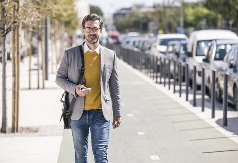 Portrait of young businessman with cell phone in the city on the go - UUF19638