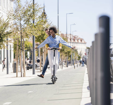 Happy young couple riding e-scooter in the city stock photo