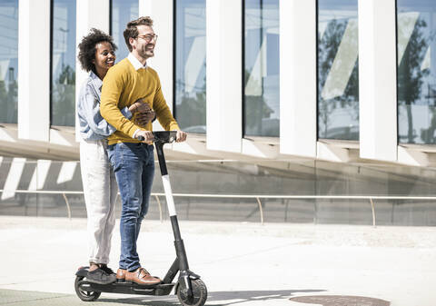 Glückliches junges Paar auf einem E-Scooter in der Stadt, lizenzfreies Stockfoto