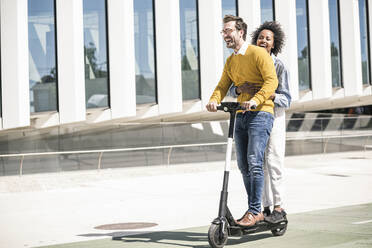 Happy young couple riding e-scooter in the city - UUF19643