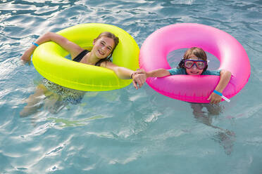 Siblings, brother and sister playing in pool with colorful floaties. - MINF12982