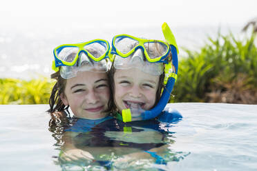 Ein Mädchen im Teenageralter und ihr 5 Jahre alter Bruder im Pool, lächelnd - MINF12987