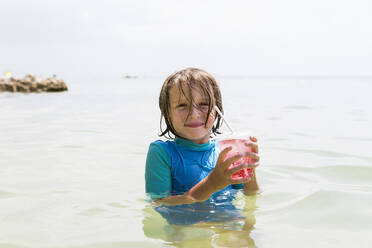 Lächelnder 5 Jahre alter Junge im Meer, mit einem Fruchtgetränk in der Hand - MINF12994