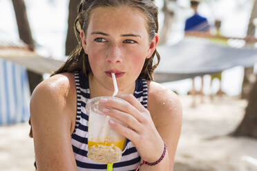 A teenage girl resting in hammock sipping fruit drink - MINF12995