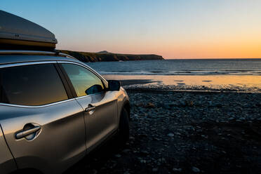 An einem Strand an der Pembrokeshire-Küste, Wales, Vereinigtes Königreich, geparktes Auto bei Sonnenuntergang. - MINF13037