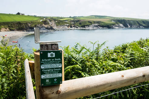 Trail signpost on Pembrokeshire Coast with cliff and bach in the background. - MINF13061