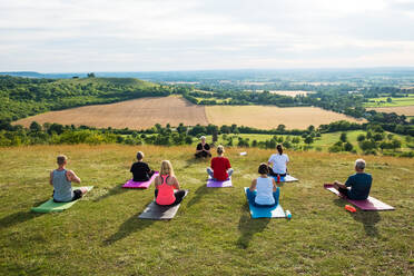 Eine Gruppe von Frauen und Männern nimmt an einer Yogastunde auf einem Hügel teil. - MINF13067