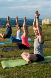 Eine Gruppe von Frauen und Männern nimmt an einer Yogastunde auf einem Hügel teil. - MINF13068