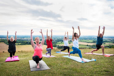 Eine Gruppe von Frauen und Männern nimmt an einer Yogastunde auf einem Hügel teil. - MINF13072