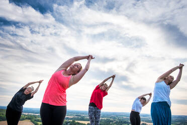 Eine Gruppe von Frauen nimmt an einer Yogastunde auf einem Hügel teil. - MINF13073