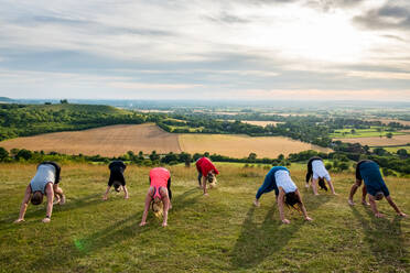 Eine Gruppe von Frauen und Männern nimmt an einer Yogastunde auf einem Hügel teil. - MINF13082