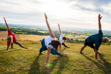 Eine Gruppe von Frauen und Männern nimmt an einer Yogastunde auf einem Hügel teil. - MINF13083