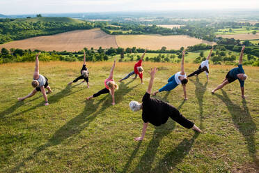 Eine Gruppe von Frauen und Männern nimmt an einer Yogastunde auf einem Hügel teil. - MINF13084