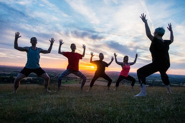 Eine Gruppe von Frauen und Männern nimmt an einer Yogastunde auf einem Hügel teil. - MINF13090