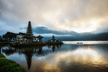 Den Sonnenaufgang auf Bali in einem Hindu-Tempel beobachten, während ein Kanu einen See überquert - CAVF68578
