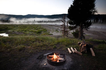 Ein morgendliches Lagerfeuer und eine Frau beim Frühstück beim Zelten am Upper Snake River auf dem John D. Rockefeller Jr. Memorial Parkway - CAVF68604