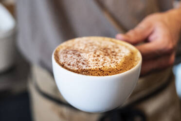 Person mit einer Tasse Cappuccino in der Hand in einer Nahaufnahme. - MINF13166