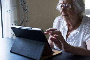 Nahaufnahme einer älteren Frau, die an einem Tisch sitzt und ein digitales Tablet mit einem Touchscreen benutzt. - MINF13179