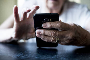 Close up of senior woman sitting at a table, using mobile phone. - MINF13180
