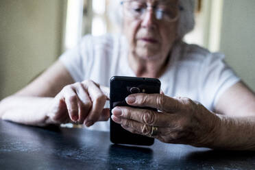 Nahaufnahme einer älteren Frau, die an einem Tisch sitzt und ein Mobiltelefon benutzt. - MINF13181