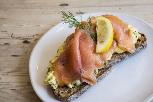 Ein offenes Sandwich auf Roggenbrot mit einem Belag aus gepökeltem Lachs oder Fisch, garniert mit einer Zitronenscheibe. - MINF13203