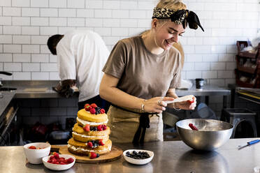 A cook working in a commercial kitchen assembling a layered sponge cake with fresh fruit. - MINF13207