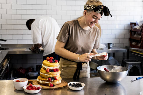 Ein Koch, der in einer Großküche arbeitet und einen geschichteten Biskuitkuchen mit frischen Früchten zusammenstellt. - MINF13207