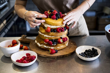 Ein Koch, der in einer Großküche arbeitet und frisches Obst auf einer Torte mit frischer Sahne anrichtet. - MINF13209