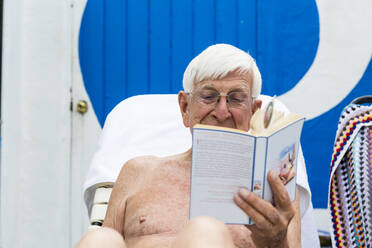 Älterer Mann am Pool, ein Buch lesend, älterer Mann liest ein Buch am Pool - MINF13241