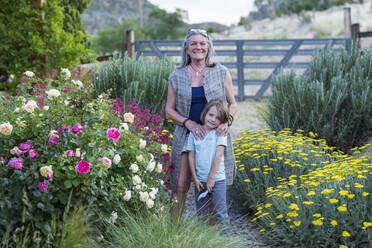 A senior adult, grandmother and her 5 year old grandson pruning roses in her garden - MINF13259