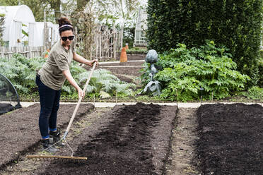 Frau harkt ein frisch angelegtes Beet in einem Gemüsegarten. - MINF13277