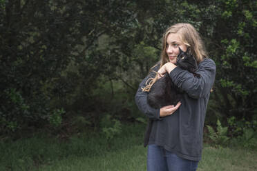 Caucasian girl with long blond hair holds black cat outside - CAVF68681