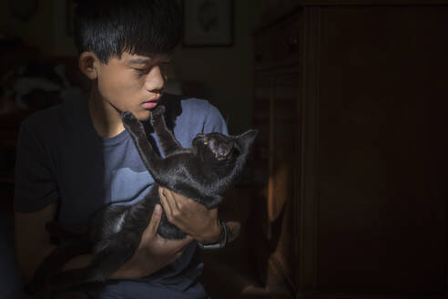 Asian Chinese boy holds black cat who touches the boy's face with paws - CAVF68682
