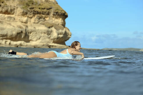 Lächelnde Frau auf dem Surfbrett liegend auf dem Meer - CAVF68721