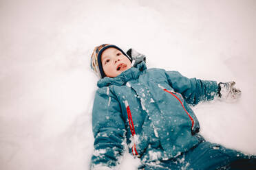 Glücklicher Junge streckt die Zunge heraus, während er im Winter im Schnee liegt - CAVF68779