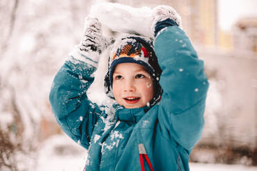 Playful boy holding chunk of snow above his head in winter - CAVF68781