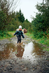 Girl standing in puddle and making spray in forest - CAVF68817