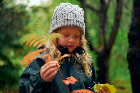 Aktives warm gekleidetes Mädchen berührt Zweig mit orangefarbenen Blättern - CAVF68829