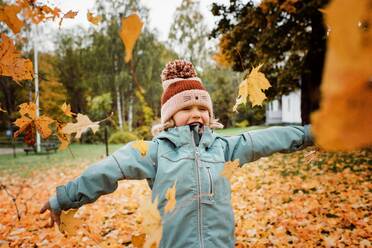 Young girl laughing and throwing fall leaves into the air - CAVF68871