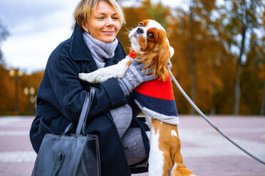 Frau auf einem Spaziergang im Park mit einem Cavalier King Charles Spaniel Hund. - CAVF68917