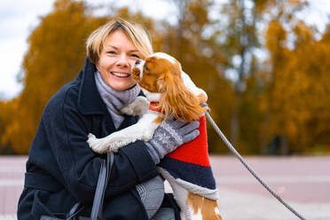 Frau lächelt im Park mit einem Cavalier King Charles Spaniel Hund. - CAVF68918