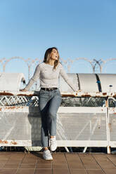 Smiling blond woman leaning on railing, looking sideways - ERRF02020