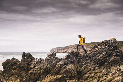 Young woman wearing yellow rain jacket at the beach, looking through binoculars, Bretagne, France stock photo