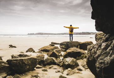 Young woman wearing yellow rain jacket at the beach at rock cave, Bretagne, France - UUF19650