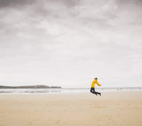 Young woman wearing yellow rain jacket at the beach, Bretagne, France stock photo