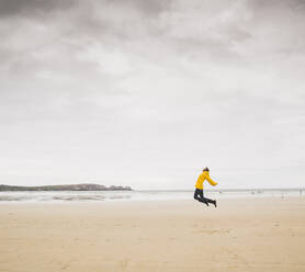 Young woman wearing yellow rain jacket at the beach, Bretagne, France - UUF19651